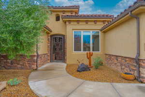 Doorway to property featuring stone siding, stucco siding, and a tiled roof