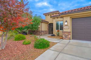 View of front of house with stucco siding, stone siding, a tiled roof, and an attached garage