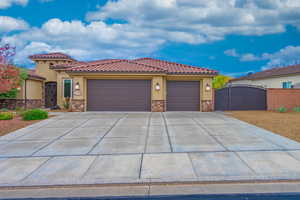 Mediterranean / spanish house with stone siding, stucco siding, and a gate