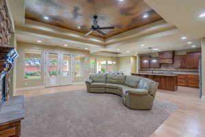 Living area with a raised ceiling, light wood-style flooring, french doors, a large fireplace, and recessed lighting