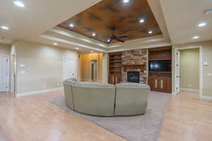 Living area with a tray ceiling, light wood-style flooring, built in features, and recessed lighting