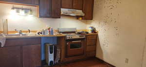 Kitchen with dark brown cabinets, range with electric stovetop, under cabinet range hood, dark tile patterned floors, and a textured wall