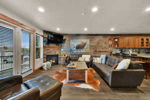 Living room with an accent wall, wood finished floors, a fireplace, recessed lighting, and wood walls