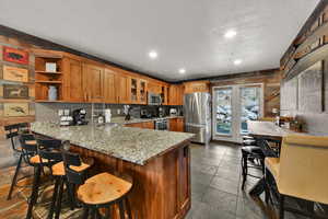 Kitchen with recessed lighting, stainless steel appliances, a peninsula, brown cabinets, and light stone countertops