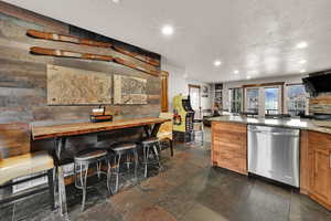 Kitchen featuring stainless steel dishwasher, light stone countertops, recessed lighting, brown cabinetry, and stone tile floors