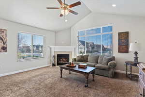 Carpeted living area featuring a tile fireplace, ceiling fan, and vaulted ceiling