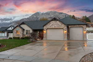 View of front of house featuring a mountain view, roof with shingles, an attached garage, concrete driveway, and stone siding