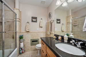 Full bath featuring vanity, tile walls, tiled shower / bath combo, a wainscoted wall, and light tile patterned flooring