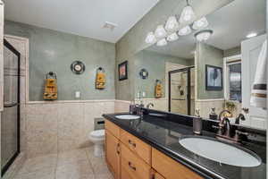 Bathroom featuring double vanity, a shower stall, tile walls, light tile patterned floors, and a wainscoted wall