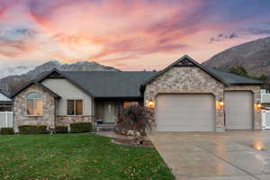 View of front of property featuring a mountain view, an attached garage, a front yard, and stone siding