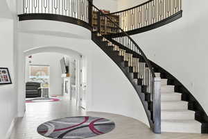 Staircase with wood finished floors, arched walkways, and a high ceiling