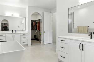 Bathroom with a walk in closet, two vanities, and a freestanding bath