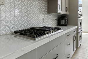Kitchen with stainless steel appliances, gray cabinetry, light stone countertops, decorative backsplash, and light wood finished floors