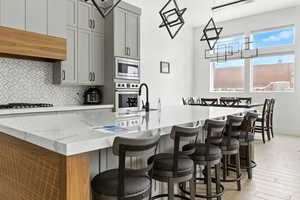 Kitchen featuring hanging light fixtures, tasteful backsplash, light wood finished floors, gray cabinets, and a center island with sink