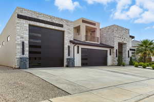 Contemporary house with stone siding, a balcony, concrete driveway, a metal roof, and a standing seam roof