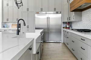 Kitchen featuring backsplash, appliances with stainless steel finishes, custom exhaust hood, and light stone countertops