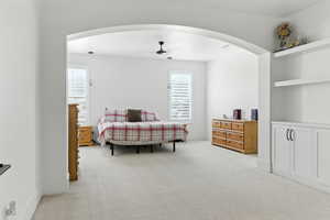 Bedroom featuring light carpet, arched walkways, and ceiling fan