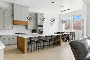 Kitchen featuring gray cabinets, an island with sink, a breakfast bar, and backsplash
