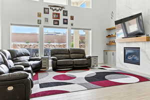 Living area with a premium fireplace, healthy amount of natural light, a towering ceiling, and light wood-type flooring