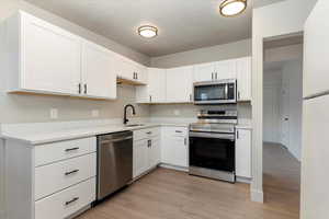 Kitchen with stainless steel appliances, white cabinets, light wood-type flooring, and a textured ceiling