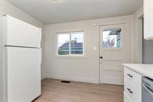Kitchen with freestanding refrigerator, white cabinets, light wood-type flooring, dishwasher, and a textured ceiling