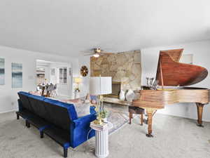 Carpeted living room with a fireplace, a textured ceiling, and ceiling fan