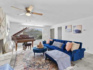Carpeted living room featuring a stone fireplace and a ceiling fan
