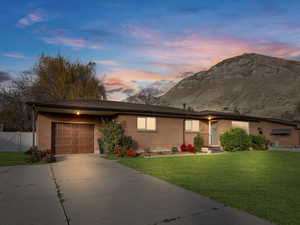 Single story home with concrete driveway, an attached garage, brick siding, a yard, and a mountain view