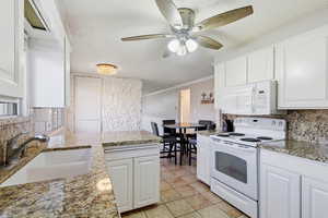 Kitchen featuring tasteful backsplash, white appliances, ornamental molding, a peninsula, and white cabinetry