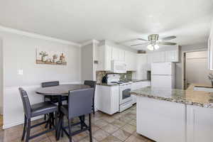 Kitchen featuring white appliances, white cabinets, a textured ceiling, decorative backsplash, and light stone countertops