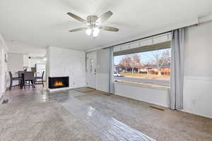 Unfurnished living room featuring a large fireplace, a textured ceiling, carpet floors, and ceiling fan