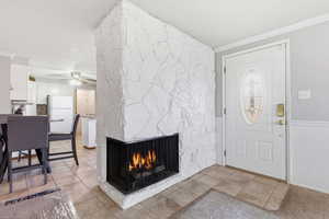 Entrance foyer with crown molding, light tile patterned floors, a multi sided fireplace, and a ceiling fan