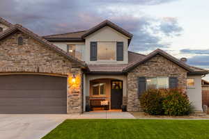 View of front of house with stone siding, stucco siding, a garage, concrete driveway, and a yard