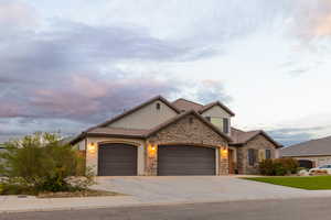View of front of home with a garage, driveway, stucco siding, a tiled roof, and stone siding