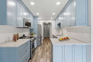 Kitchen with stainless steel appliances, tasteful backsplash, light stone countertops, light wood-style floors, and recessed lighting