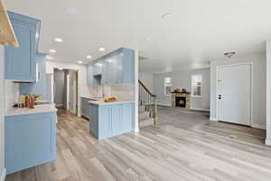 Kitchen featuring open floor plan, light stone countertops, a fireplace, range hood, and light wood-style floors