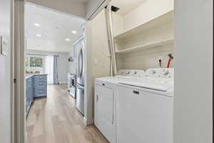 Laundry room featuring light wood-style flooring, washer and clothes dryer, and recessed lighting