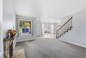 Foyer featuring stairs, a stone fireplace, and light colored carpet