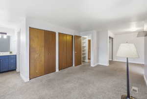 Unfurnished bedroom with ensuite bath, multiple closets, and light colored carpet