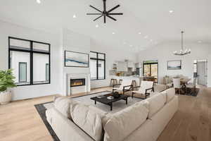 Upper level great room featuring a glass covered gas fireplace, light wood finished floors, high vaulted ceiling, recessed lighting, and ceiling fan (virtual staging)