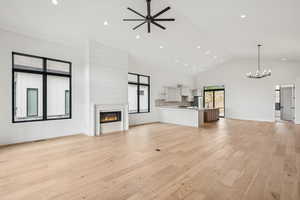 Upper level great room featuring a glass covered gas fireplace, light wood finished floors, high vaulted ceiling, recessed lighting, and ceiling fan