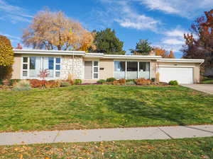 View of front of home with brick siding, a front lawn, a chimney, a garage, and driveway