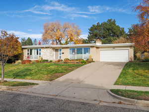 View of front facade with a chimney, concrete driveway, brick siding, a front yard, and an attached garage