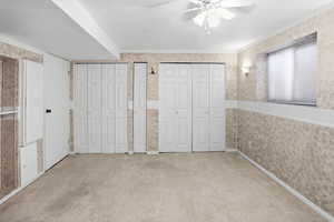 Unfurnished bedroom featuring wallpapered walls, two closets, ceiling fan, and carpet flooring