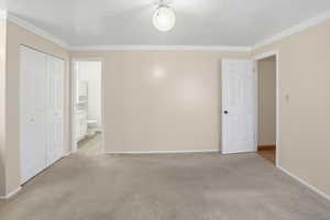 Unfurnished bedroom featuring a closet, light colored carpet, crown molding, and ensuite bathroom