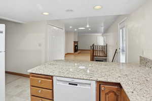 Kitchen featuring light stone counters, white appliances, brown cabinets, a peninsula, and recessed lighting