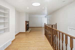 Corridor featuring light wood-style floors, recessed lighting, and an upstairs landing