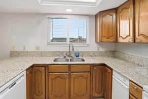 Kitchen with brown cabinets, light stone counters, white dishwasher, and crown molding