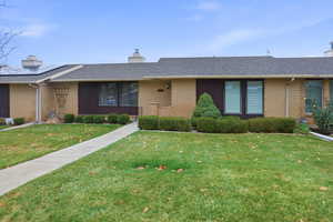 Ranch-style home with a shingled roof, a chimney, a front yard, and brick siding