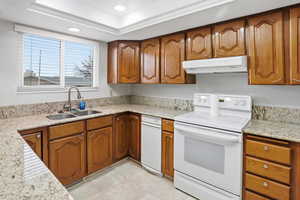 Kitchen featuring brown cabinetry, light stone countertops, electric stove, under cabinet range hood, and recessed lighting
